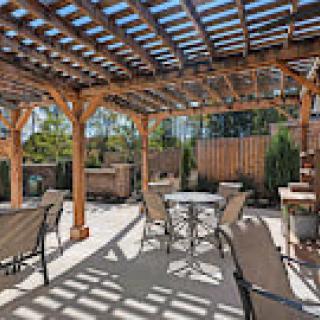 A sunny outdoor patio with a wooden pergola, featuring comfortable seating and a table.