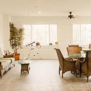 A cozy living room with a sofa, dining table, and chairs, featuring large windows and an indoor plant.