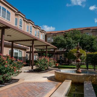 A serene residential courtyard featuring a landscaped garden and a central fountain under a clear blue sky.