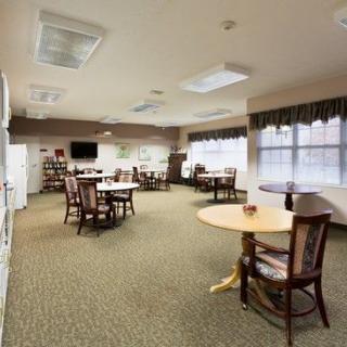 An empty room with several round tables and chairs, well-lit by natural light coming through large windows.