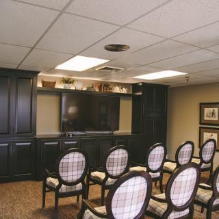 A small conference room with rows of upholstered chairs facing a large television, surrounded by wooden cabinetry.