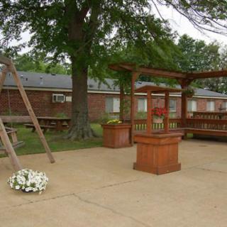 A peaceful outdoor garden area featuring a wooden pergola, swing, and potted flowers.