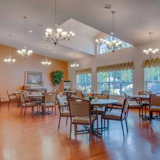 A bright and spacious dining room with multiple tables and chairs, featuring large windows and elegant chandeliers.