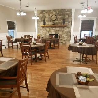 A cozy dining room with neatly arranged tables and chairs, featuring a stone fireplace as the focal point.