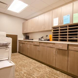 A modern office breakroom featuring cabinets, a printer, and organized mail slots.