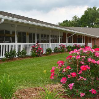 A building with a white porch surrounded by vibrant flowers and greenery.