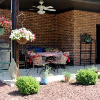 A cozy patio area with a table and chairs, surrounded by plants and flowers, against a brick wall backdrop.