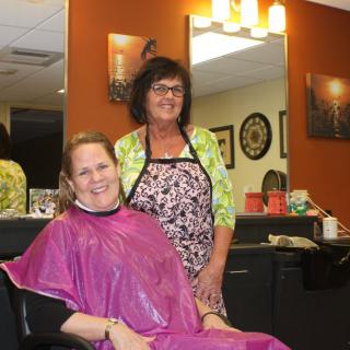 A hairstylist with a client in a hair salon, both smiling for the camera.