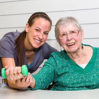 A caregiver assists an elderly woman with physical therapy exercises.