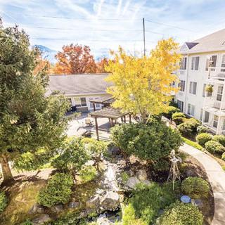 A serene courtyard with lush gardens surrounded by a multi-story building, featuring vibrant autumn foliage.
