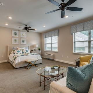 A modern bedroom with neutral tones, featuring a cozy bed, ceiling fans, and stylish furniture.