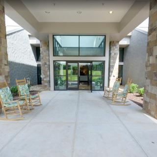 A modern building entrance with rocking chairs facing glass doors.