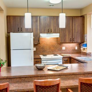 A modern kitchen with wooden cabinets, white refrigerator and stove, featuring pendant lighting and a countertop seating area.