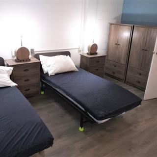 A modern bedroom with two single beds, nightstands, and a wardrobe.