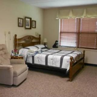 A cozy bedroom with a wooden bed, a comfortable armchair, and a window with blinds.