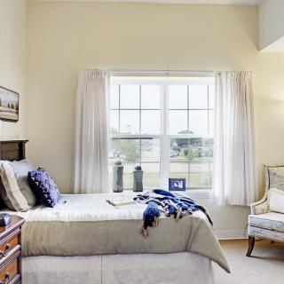 A cozy bedroom with natural light streaming in through a large window, featuring a neatly made bed and simple decor.