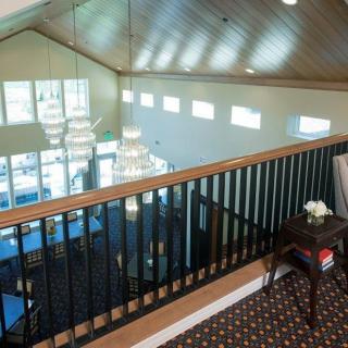 View from a mezzanine overlooking a well-lit room with large windows and elegant furnishings.