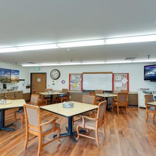 A classroom with tables, chairs, and a whiteboard, featuring a wooden floor and educational posters.