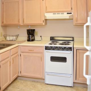 A cozy kitchen with light wooden cabinets, a stove, and a coffee maker on the countertop.