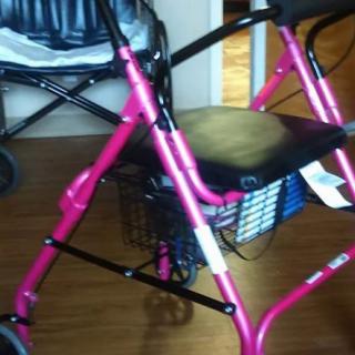 A pink mobility walker with a seat and basket indoors.