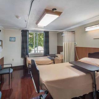A clean and empty hospital room with two neatly made beds separated by a curtain, featuring a window looking outside.