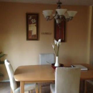 A cozy dining room featuring a wooden table, upholstered chairs, artwork on the walls, and a decorative chandelier overhead.