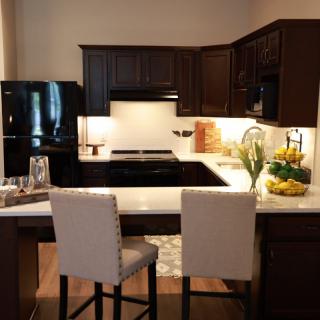 A modern kitchen with dark wood cabinets and black appliances, featuring a cozy seating area with bar stools.