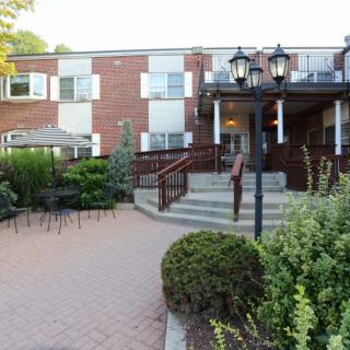 A brick building with outdoor seating and well-maintained landscaping, featuring stairs leading to the entrance.