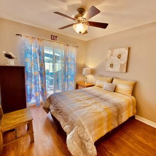 A cozy bedroom with a neatly made bed, ceiling fan, wooden furniture, and soft lighting.