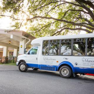A shuttle bus parked outside a facility, surrounded by greenery.