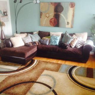 A cozy living room featuring a large brown sofa with multiple cushions, a modern rug with circular patterns, and abstract artwork on the wall.