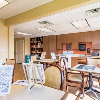 A well-lit art room with tables and easels, featuring a kitchen area in the background.