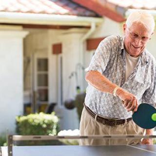 A senior man playing table tennis outdoors, enjoying a leisurely game.