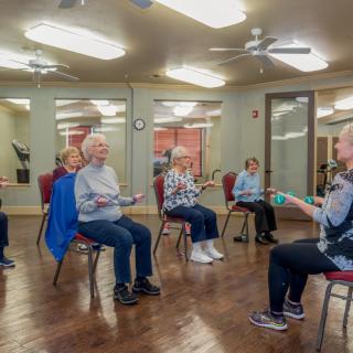 A group of senior citizens participating in a chair exercise class indoors.