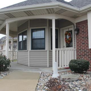 A welcoming porch with a decorative wreath, showcasing a blend of brick and siding on a beautiful residential home.