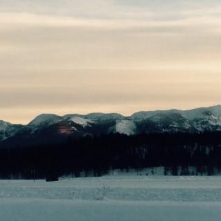 A serene winter landscape with snow-covered mountains at sunset.