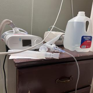 A bedside setup featuring a CPAP machine alongside a water jug and some cables.
