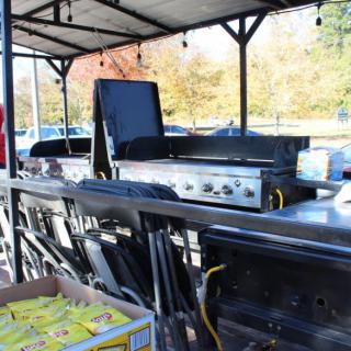 Outdoor grilling setup under a shelter with cooking equipment and autumn background.
