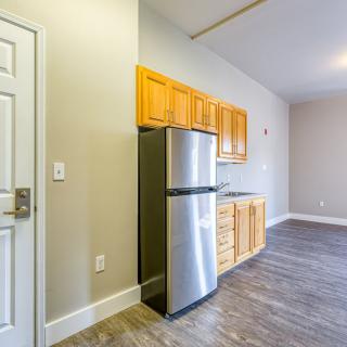 A modern apartment kitchen with wooden cabinets and a stainless steel refrigerator.