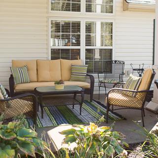 A cozy outdoor patio setup with a sofa, chairs, table, and cushions beside a house.