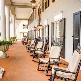A row of rocking chairs on a spacious porch with columns and lanterns.