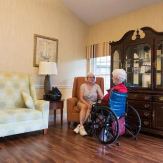 Two elderly individuals sit in a comfortable living room, engaged in conversation.