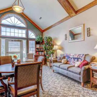 A cozy living room with a vaulted ceiling, featuring a sofa, dining table, and chairs next to large windows.