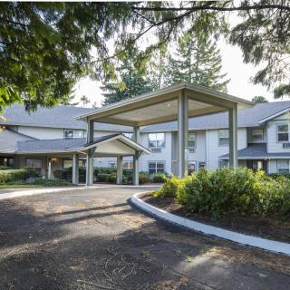 A residential building with a large driveway and surrounded by trees.