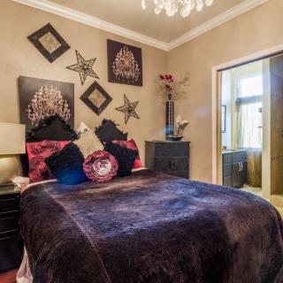 A cozy bedroom with elegant decor and a plush comforter, featuring stylish artwork and a chandelier.