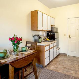 A cozy kitchen with a dining table set for two, featuring green tableware and a bouquet of red flowers.