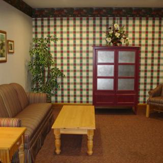 A cozy living room with plaid wallpaper, featuring a sofa, armchair, coffee table, and a red cabinet.