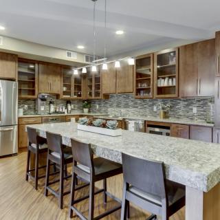 A modern kitchen featuring wood cabinets, a large granite island with bar stools, and stainless steel appliances.