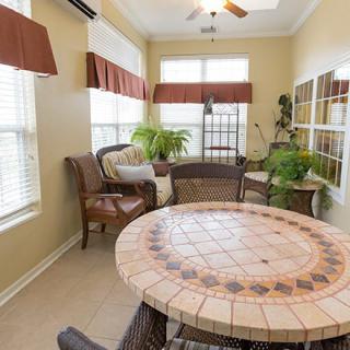 A cozy sunroom with wicker furniture, a round tiled table, and lush indoor plants.