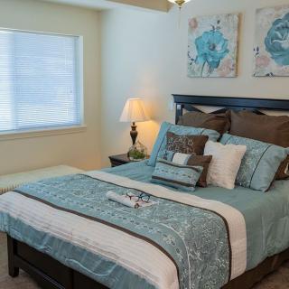A cozy bedroom with teal and brown bedding, decorative pillows, and wall art.